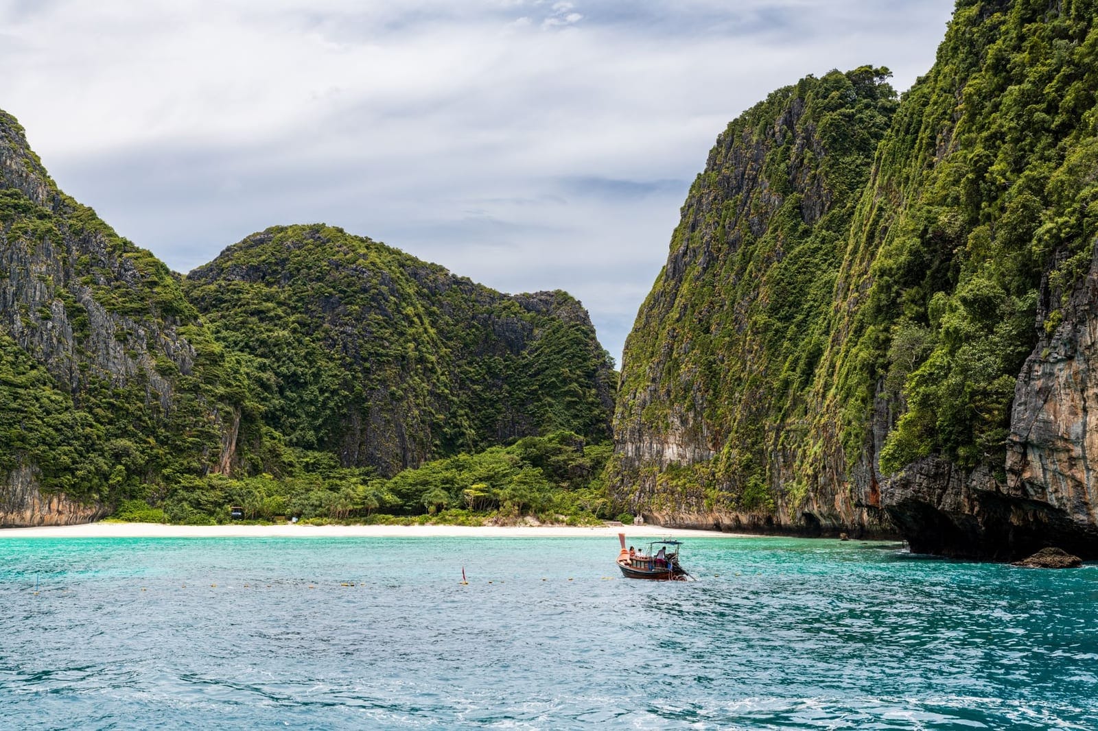 Longtail boat in turquoise water below limestone cliffs